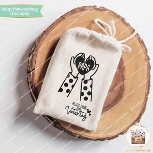 May include: A white fabric bag with a black and white illustration of two hands holding a heart with the word "PAPA" inside. The text "ALLES LIEBE ZUM VATERTAG" is printed below the illustration.