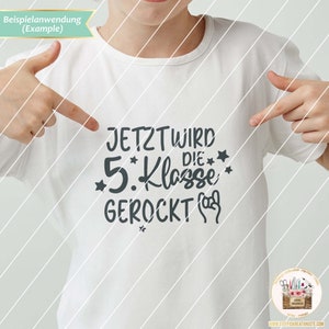 May include: White t-shirt with the text "JETZT WIRD DIE 5. KLASSE GEROckt" in gray lettering with stars and a rock and roll hand gesture.