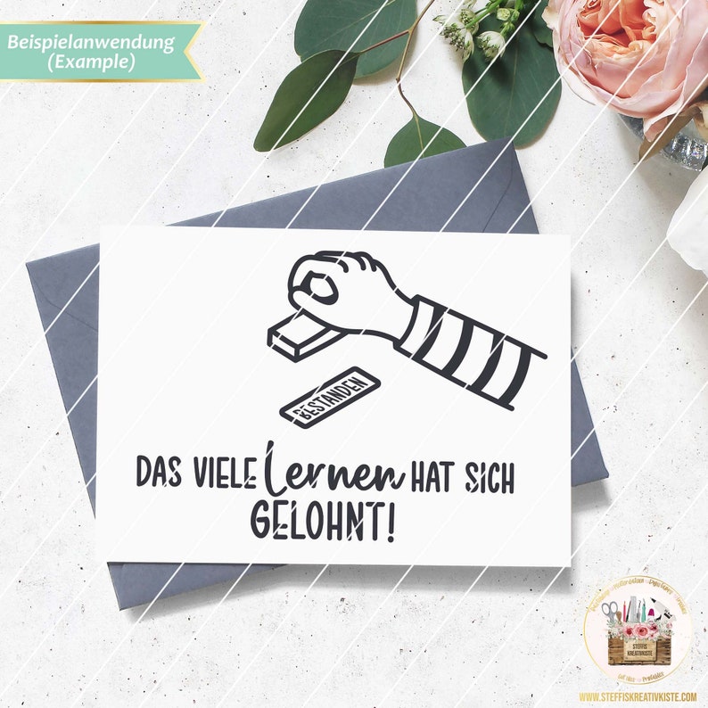 May include: A black and white illustration of a hand stamping a piece of paper with the word "Bestanden" on it. The text below the illustration reads "Das viele lernen hat sich gelohnt!"