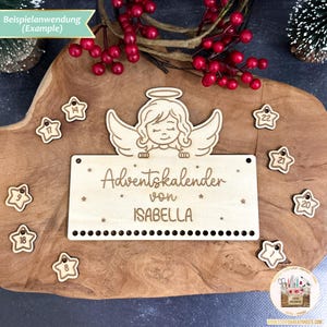 May include: A wooden Advent calendar with a cutout angel design. The calendar is personalized with the name "ISABELLA" and the text "Adventskalender von". The calendar has 24 numbered wooden stars for each day of Advent.