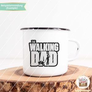 Op de afbeelding: Een witte emaille mok met een zwart handvat. De mok heeft een zwart-witte afbeelding met de tekst "The Walking Dad" en een silhouet van een persoon die een kruiwagen duwt.