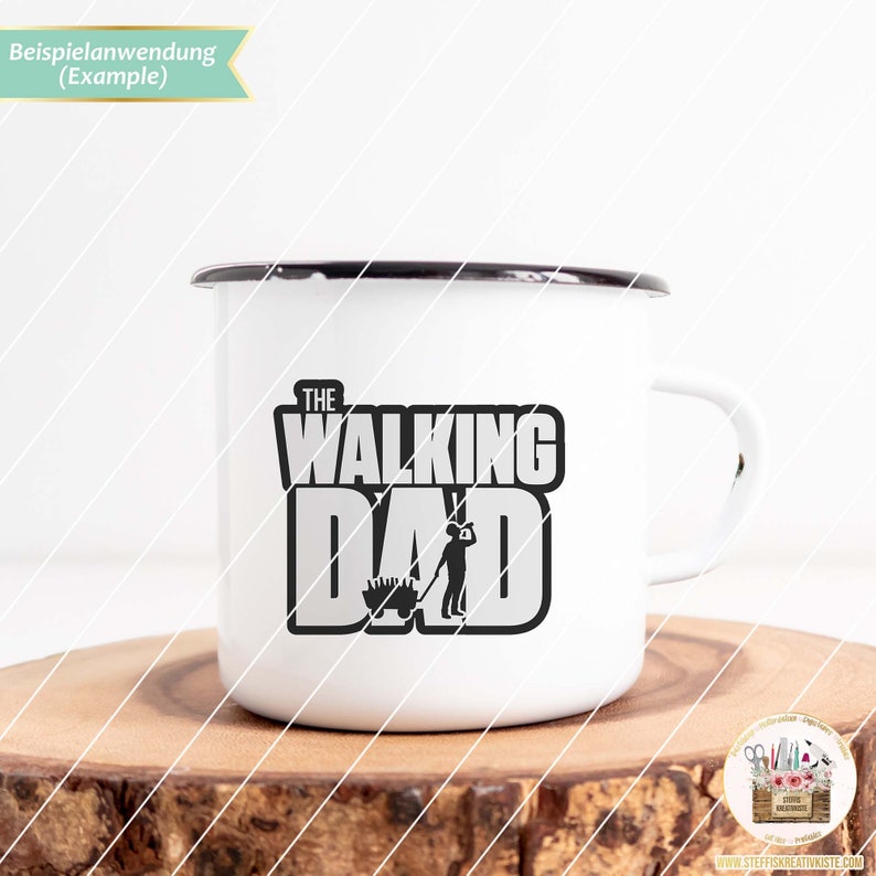 Op de afbeelding: Een witte emaille mok met een zwart handvat. De mok heeft een zwart-witte afbeelding met de tekst "The Walking Dad" en een silhouet van een persoon die een kruiwagen duwt.