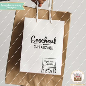 May include: A white gift bag with black text that reads "Geschenk zum Abschied" and a small black heart. The bag also has a black and white illustration of a person holding a sign that reads "F&uuml;r die beste Lehrerin!"