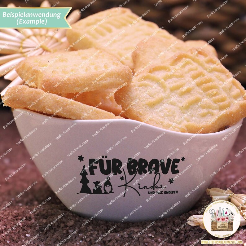 May include: A white ceramic bowl filled with shortbread cookies. The bowl has a black design that says "F&uuml;r Brave Kinder" and "Und Alle Anderen".