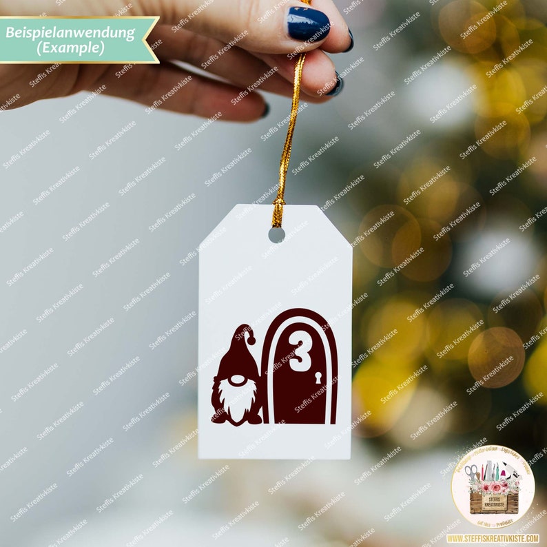 May include: A white tag with a brown gnome and a brown door with the number 3 on it. The tag is hanging from a gold string.