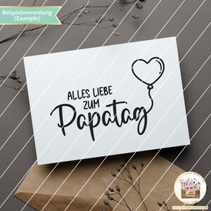 May include: A white card with black text that reads "Alles Liebe zum Papa Tag" with a heart-shaped balloon above the text.