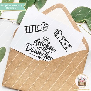 May include: A white card with a black and white illustration of two fists bumping. The text "Wir dr&uuml;cken dir die Daumen" is written below the fists.