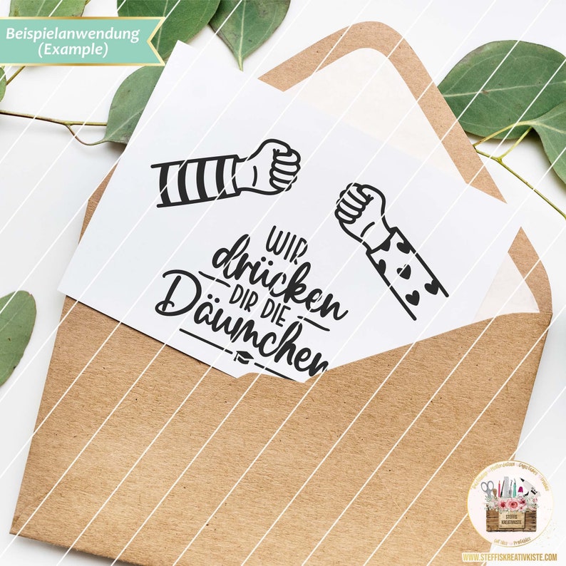 May include: A white card with a black and white illustration of two fists bumping. The text "Wir dr&uuml;cken dir die Daumen" is written below the fists.