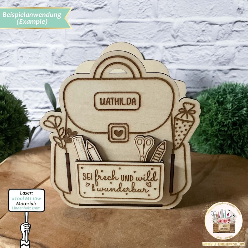 May include: A wooden cutout of a backpack with the name "MATHILDA" on the front. The backpack has a pocket with the text "SEI frech UND wild & wunderbar" on it. The backpack is made of 3mm linden wood and was cut with a xTool M1 10W laser.