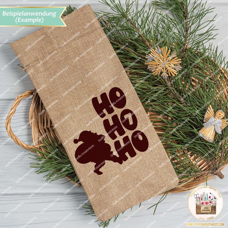 May include: A brown burlap gift bag with a red Santa Claus silhouette and the text "HO HO HO" printed on it. The bag is sitting on a woven basket with a pine branch in the background.