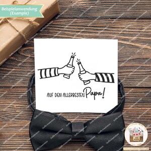 May include: A white card with a black ink illustration of two people clinking beer bottles. The text reads "AUF DEN ALLERBESTEN Papa!"