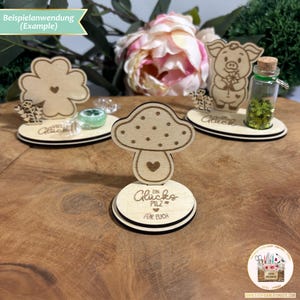 May include: Three wooden decorations with a mushroom, a four-leaf clover, and a pig. Each decoration has a small heart and the text "Gl&uuml;ck" (German for "luck") on it. The mushroom decoration also has the text "Ein Gl&uuml;ckspilz f&uuml;r Euch" (German for "A lucky mushroom for you").