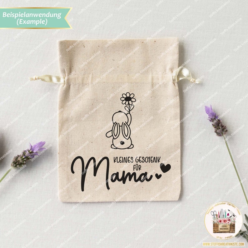 May include: A white drawstring bag with a black bunny holding a flower and the text "KLEINES GESCHENK FUR Mama" with two hearts.