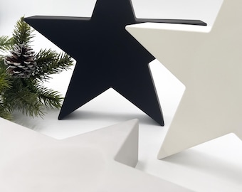 May include: Three-dimensional star decorations in black and white. The stars are arranged in a group, with a sprig of evergreen and a pinecone in the background. These decorative stars are suitable for holiday or seasonal decor.