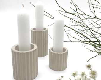 May include: Three beige concrete candle holders with white candles. The candle holders have a ribbed design.