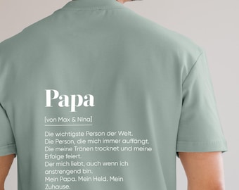 May include: A light green t-shirt with the German word "Papa" in large white letters. Below the word is the text "[von Max & Nina]" and a list of phrases in German. The shirt is a crew neck.