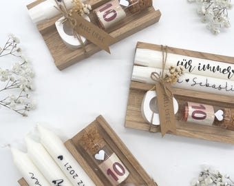 May include: Three wooden boxes with white candles, a small glass vial with a cork stopper, and a heart-shaped piece of wood. The boxes are decorated with the text "15. MÄRZ 2021", "wir immer", and "Alles Liebe".