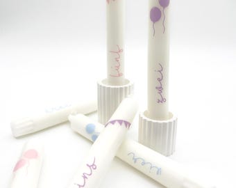 May include: Five white tubes with colorful designs and text. The tubes have the words "pink", "blue", "eins", "zwei", and "drei" written on them. The designs include balloons, flags, and swirls.