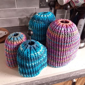 Puede incluir: Cuatro agarraderas de olla de ganchillo en diferentes colores y patrones. Las agarraderas de olla son azules, verde azulado, rosas y moradas. Todas están hechas con un punto texturizado.