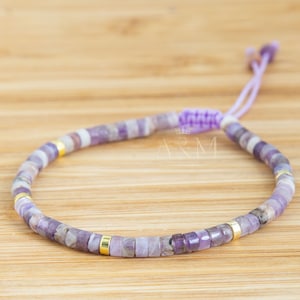 以下が含まれることがあります： 紫と金のビーズで作られたブレスレットで、スライド式の結び目の留め具が付いています。ブレスレットは、小さなファセットカットの紫水晶のビーズと金色のスペーサーで作られています。