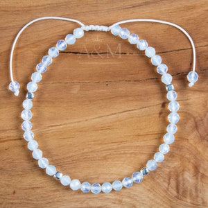 May include: A white beaded bracelet with silver accents. The bracelet is made of small, faceted beads and is tied with a white cord.