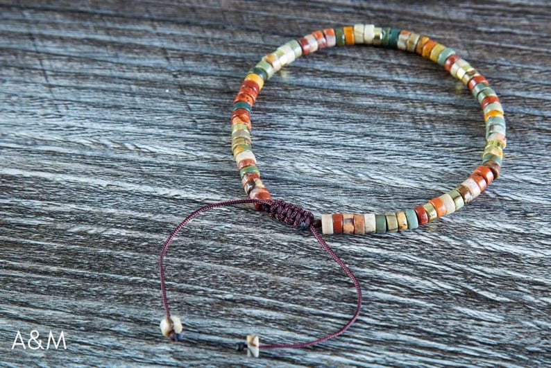 May include: A multi-colored beaded bracelet with a brown cord closure. The beads are made of various shades of brown, red, green, and white.