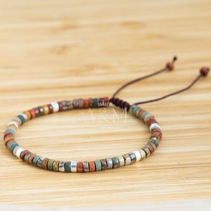 May include: A brown leather cord bracelet with multi-colored stone beads and silver beads. The bracelet is adjustable with a sliding knot.