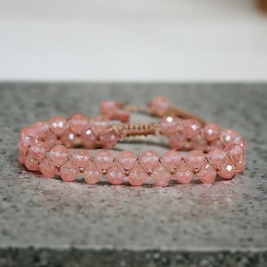 Puede incluir: Un brazalete de cuentas rosadas con cierre anudado. Las cuentas son facetadas y tienen un brillo sutil.