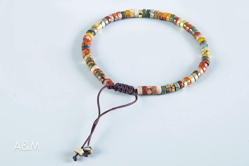 May include: A multi-colored beaded bracelet with a brown cord closure. The beads are made of various stones and have a natural, earthy look.