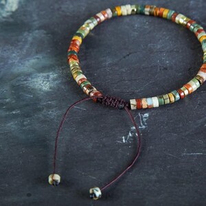 May include: A multi-colored beaded bracelet with a brown cord closure. The beads are made of various stones and have a natural, earthy look.