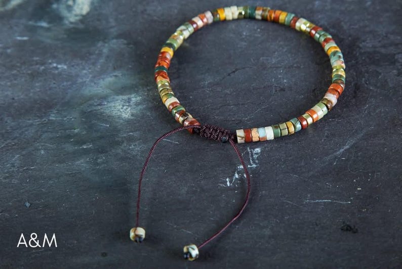 May include: A multi-colored beaded bracelet with a brown cord closure. The beads are made of various stones and have a natural, earthy look.