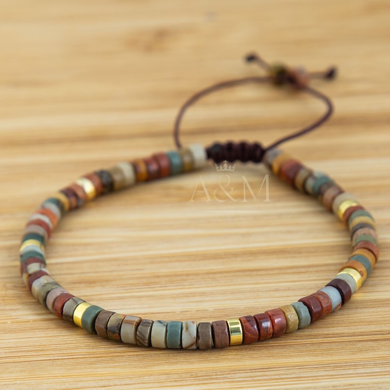 May include: A multi-colored beaded bracelet with a brown cord closure. The beads are made of natural stone and have a variety of colors, including red, brown, green, and gold. The bracelet is adjustable and can be worn by both men and women.