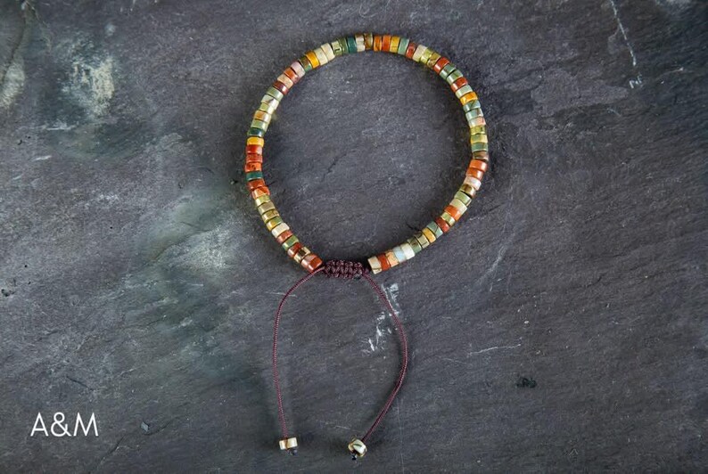 May include: A multi-colored beaded bracelet with a brown cord and a sliding knot closure. The beads are small and round, and they are arranged in a random pattern. The bracelet is made of natural materials.