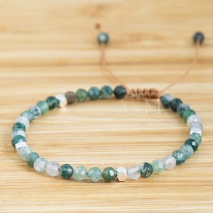 May include: A green and white agate gemstone bracelet with silver accents and a brown adjustable cord.