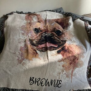 May include: A woven throw blanket with a watercolor-style image of a French Bulldog. The blanket has a fringe border and the name "Brownie" is embroidered in black on the bottom.