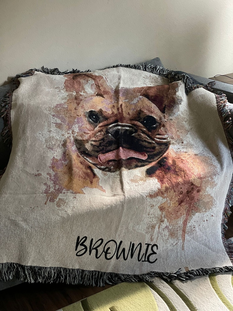 May include: A woven throw blanket with a watercolor-style image of a French Bulldog. The blanket has a fringe border and the name "Brownie" is embroidered in black on the bottom.