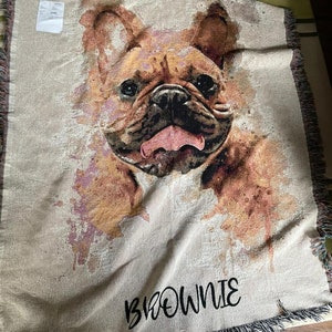 May include: A woven throw blanket with a watercolor-style image of a French Bulldog. The dog's tongue is sticking out and the blanket has the name "BROWNIE" embroidered on it.