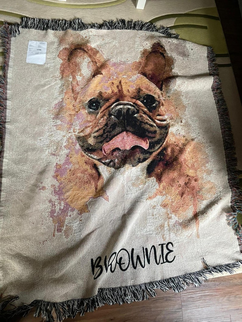 May include: A woven throw blanket with a watercolor-style image of a French Bulldog. The dog's tongue is sticking out and the blanket has the name "BROWNIE" embroidered on it.