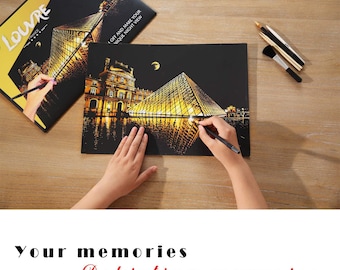 Puede incluir: Un lienzo negro con un diseño de pintura por números metálico dorado de la Pirámide del Louvre en París. El lienzo está sobre una mesa de madera con una persona usando un estilete negro para pintar el diseño. El lienzo tiene las palabras "DIY and make your unique night view" impresas en él.