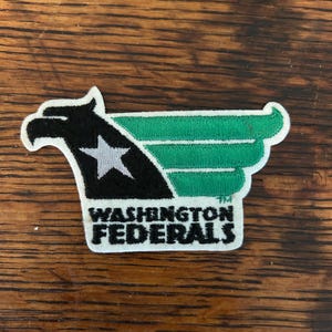 May include: Embroidered patch featuring a stylized eagle head in black and green with a white star. The patch reads "WASHINGTON FEDERALS" in white block letters. The patch is rectangular with a white border.