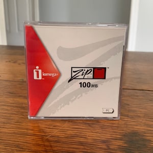 May include: A clear plastic case containing a red and white Iomega Zip 100MB disk. The disk is labeled "Zip Brand" and "100MB". The case also has a label that says "PC".
