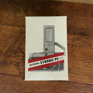 May include: A white box with a black and white illustration of a National Strobo PE-3R flash unit. The box has red text that says "National Strobo PE-3R".