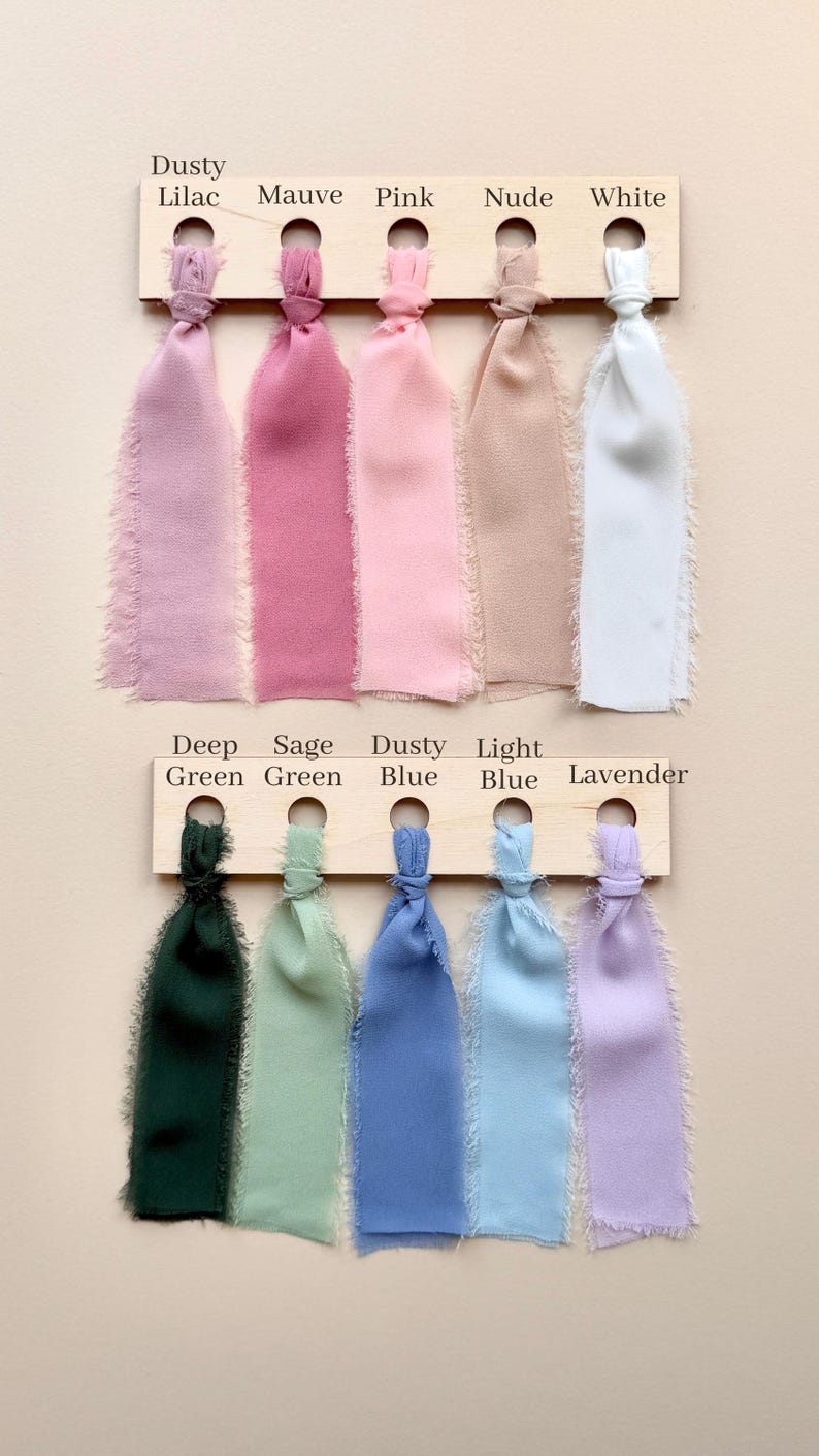 Puede incluir: Dos tablas de madera que sostienen diez cintas de tela con bordes deshilachados en varios colores. La fila superior presenta Dusty Lilac, Mauve, Pink, Nude y White. La fila inferior muestra las etiquetas Deep Green, Sage Green, Dusty Blue, Light Blue y Lavender.
