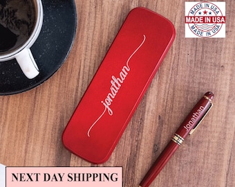 May include: A red metal pen case with the name "jonathan" engraved on it. A red pen with gold accents and the name "jonathan" engraved on it is next to the case. The pen and case are on a wooden surface. The image also includes a "Made in USA" label.