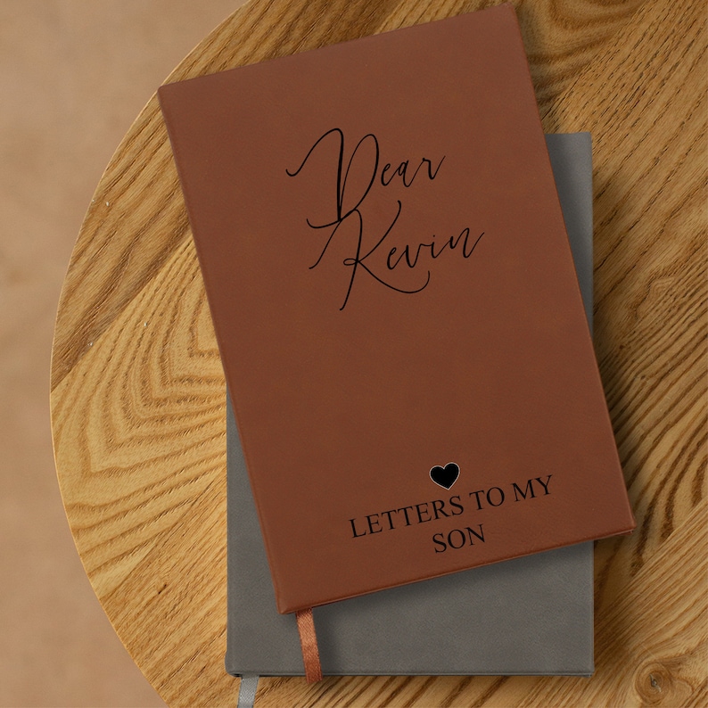 May include: A brown leather journal with the text "Dear Kevin" and "Letters to My Son" on the cover. A heart symbol is above the text "Letters to My Son".