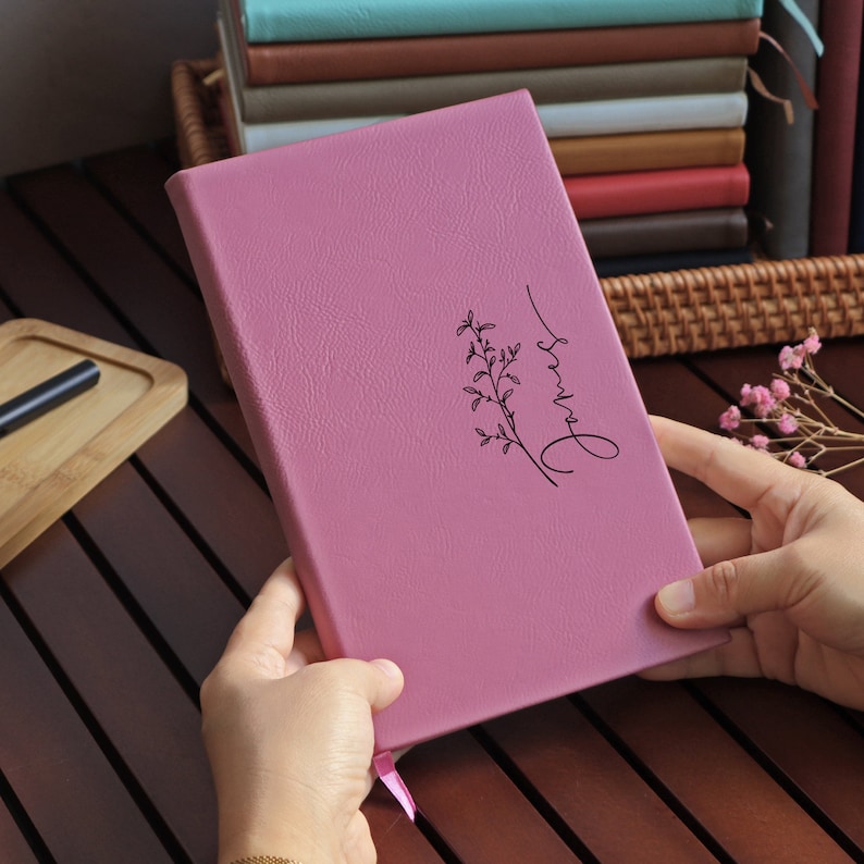 May include: A pink leather-bound journal with a floral design and the word "always" written in cursive on the front cover.