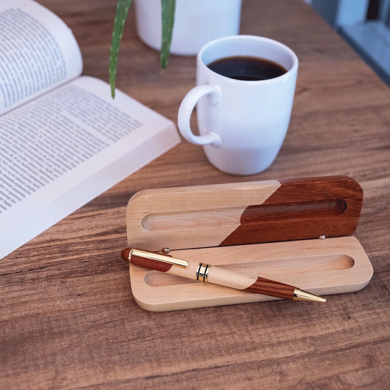 May include: A wooden pen case with a brown and natural wood finish. The case is open and a wooden pen with gold accents is inside.