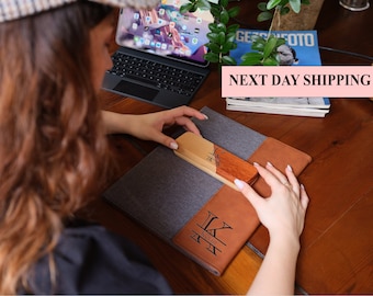 May include: A brown leather and gray fabric notebook with the initials "K.Y." and the word "Kevin" engraved on the front. The notebook is closed and lying on a wooden table. A wooden bookmark with the initials "K.Y." is placed on the notebook.