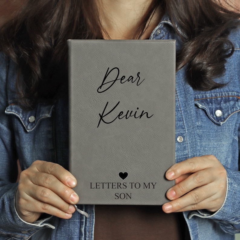 May include: Grey leather journal with the text "Dear Kevin Letters to My Son" and a small black heart.