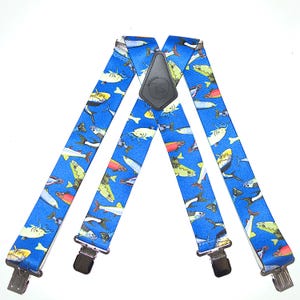 May include: Blue suspenders featuring a pattern of various colourful fish. The suspenders have silver clips and a black leather patch. The fish are depicted in yellow, red, and white, creating a vibrant design.